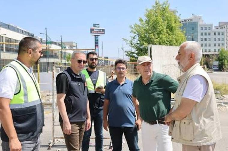 Şantiye alanında reflektif yelekli iki kişi ve dört kişi, açık havada bir arada duruyor.