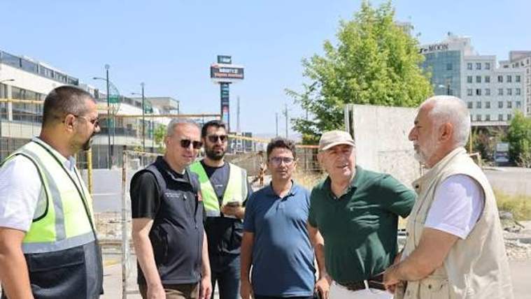 Şantiye alanında reflektif yelekli iki kişi ve dört kişi, açık havada bir arada duruyor.