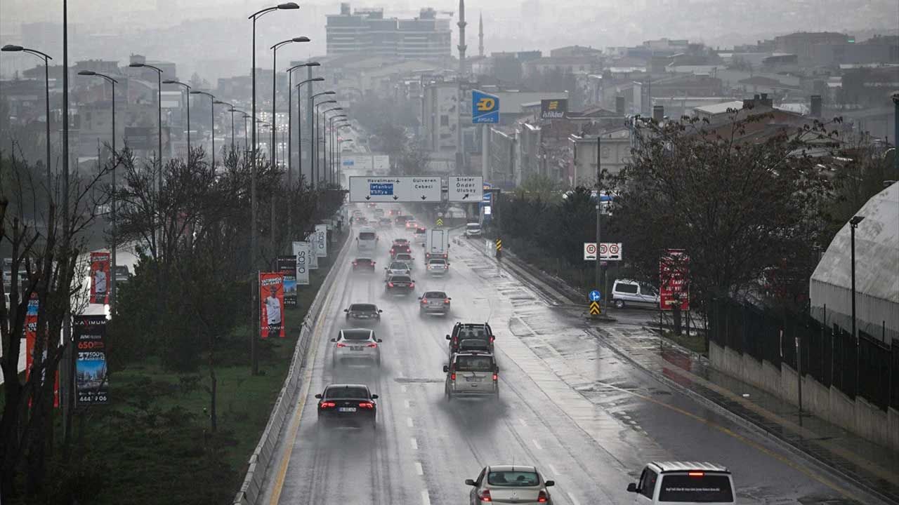 Yağmur altında, ıslak bir yolda ilerleyen araçlar ve etrafta ağaçlar görünmektedir.