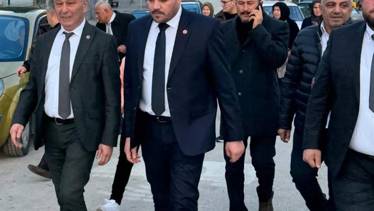 Bir grup insan, sokakta yürüyerek ilerliyor; ön planda takım elbise giymiş bir adam var.