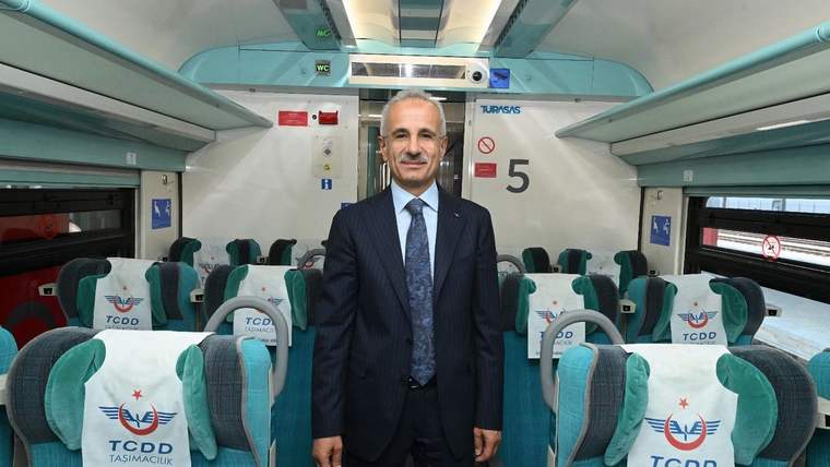 TCDD Taşımacılık yazılı koltukların bulunduğu tren vagonunda takım elbiseli bir kişi ayakta duruyor.