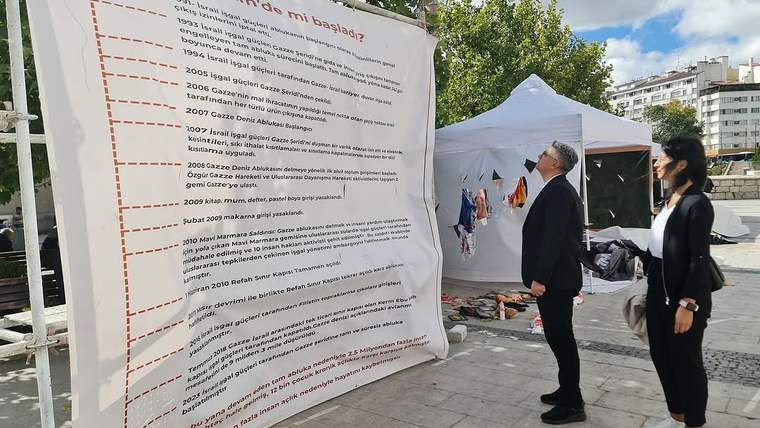 Bir adam ve bir kadın, açık alanda sergilenen büyük bir afişe bakıyorlar.