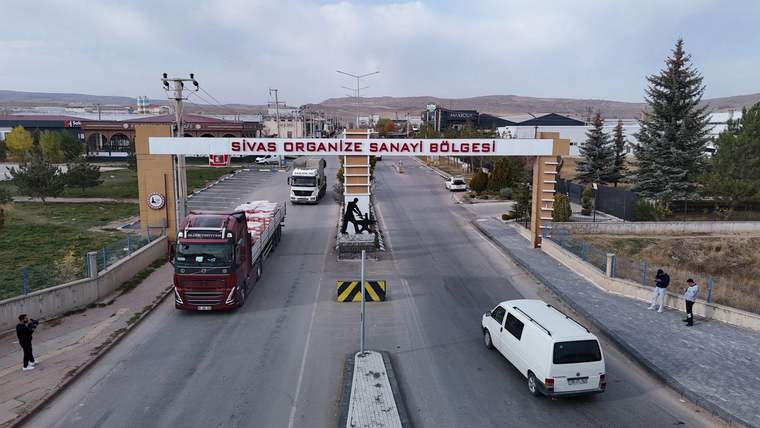 Üzerinde “Sivas Organize Sanayi Bölgesi” yazan giriş takının altında kamyon ve minibüslerin bulunduğu yol