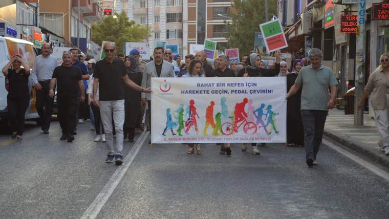 Kent sokağında yürüyen kalabalık, üzerinde bisikletli figürler ve slogan bulunan pankartı taşıyor.