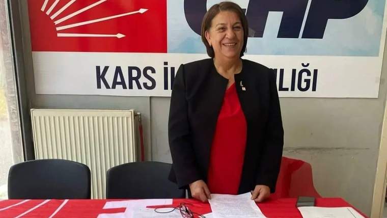 Kırmızı örtülü masada belgelerin önünde duran kadın, arkasındaki duvarda parti logosu ve yazısıyla görülüyor.