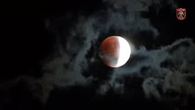 Bulutlu gece gökyüzünde, bir yanı kızıl diğer yanı aydınlık görünen Ay tutulması