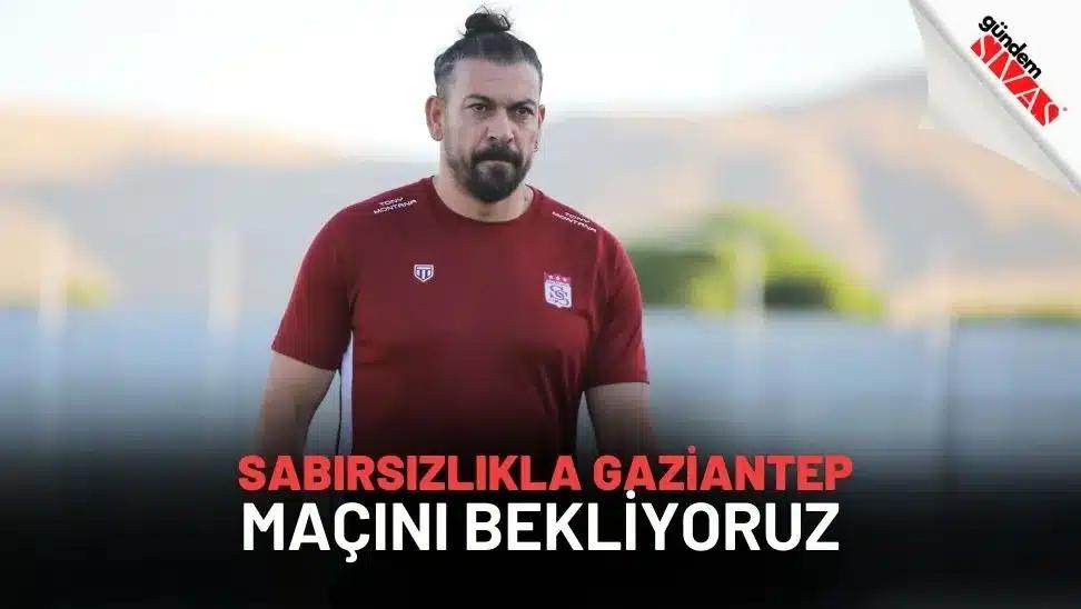 Topuz saçlı bir kişi, bordo spor formasıyla bulanık bir saha arka planında ayakta duruyor.