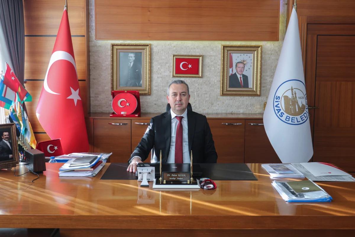 Sivas Belediye Başkanı Adem Uzun, makamında oturuyor, arkasında Türk bayrağı ve Sivas Belediyesi logosu var.