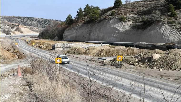 Dağlık arazide yapımı süren yolda bir otomobil, 70 hız sınırı levhaları ve yol çalışması görülüyor.