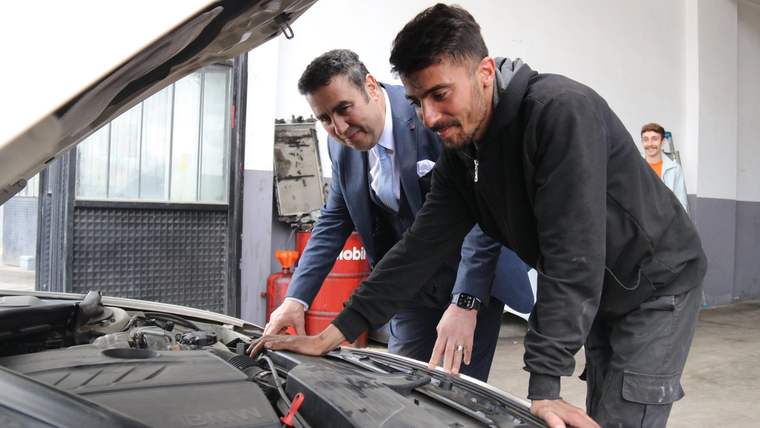 Bir kişi, otomobilin motor bölümünde inceleme yaparken yanında başka bir kişi duruyor.