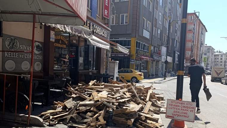 İş yerlerinin önündeki kaldırımda tahta parçalarından oluşan büyük bir yığın, yanında uyarı levhası bulunuyor.