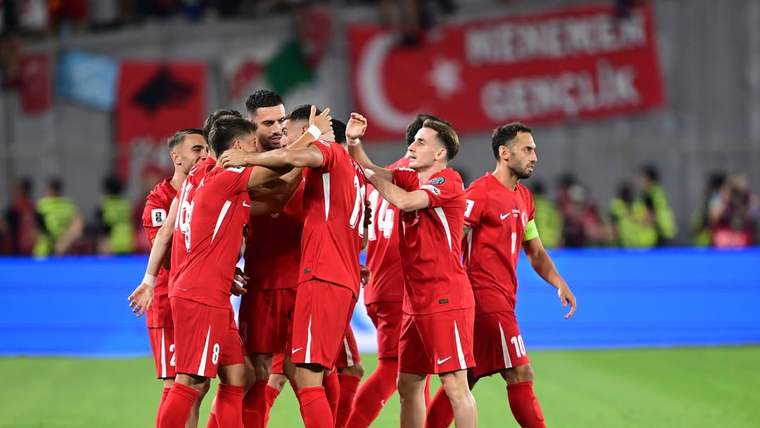 Kırmızı formalar giyen futbolcular, saha içinde bir araya gelerek birbirlerine sarılıyor.