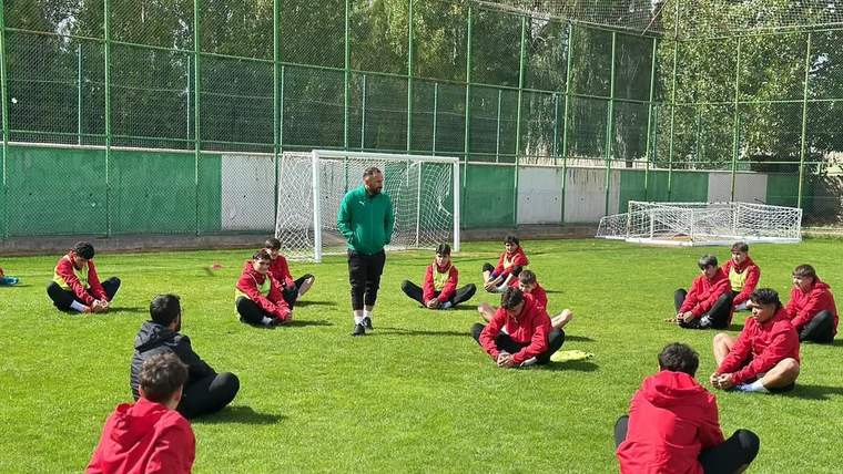 Futbol sahasında, antrenörün önünde oturan U19 futbol takımı oyuncuları, antrenman yapıyor.