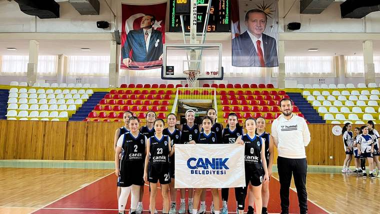 Basketbol sahasında, üzerinde “Canik Belediyesi” yazılı pankart tutan oyuncular ve bir erkek yan yana duruyor.