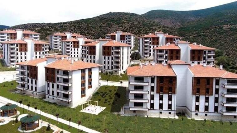 Kırmızı çatılı çok katlı konut binaları, yeşil alanlar ve dağ yamacının önünde sıralanıyor.
