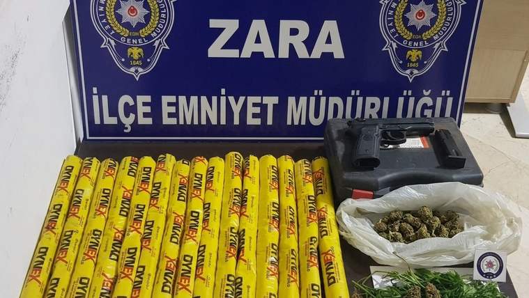 Zara İlçe Emniyet Müdürlüğü tabelası önünde sarı çubuklar, siyah kutu ve poşetlerde yeşil bitkiler duruyor.