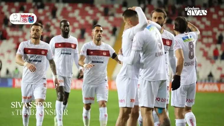 Sivasspor futbol takımı, beyaz ve kırmızı formalarıyla sahada bir araya gelmiş, oyuncular birbirine sarılıyor.