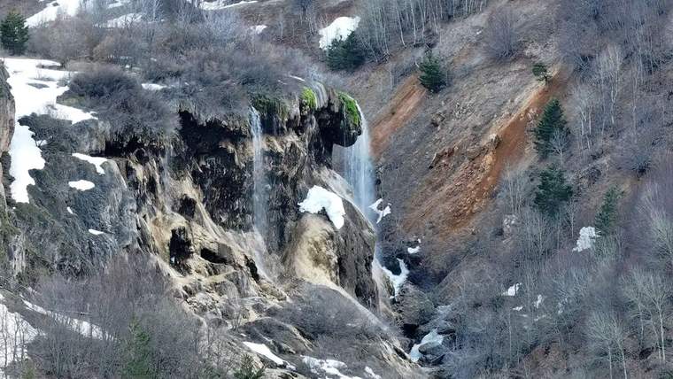 Dipsiz Göl Şelalesi'nden akan su, çevresindeki kayalık alan ve ağaçlarla birlikte görünmekte.