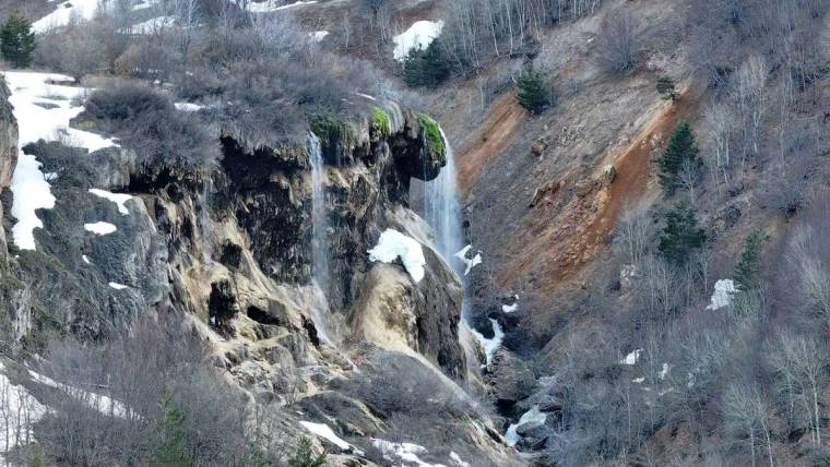 Dipsiz Göl Şelalesi'nden akan su, çevresindeki kayalık alan ve ağaçlarla birlikte görünmekte.
