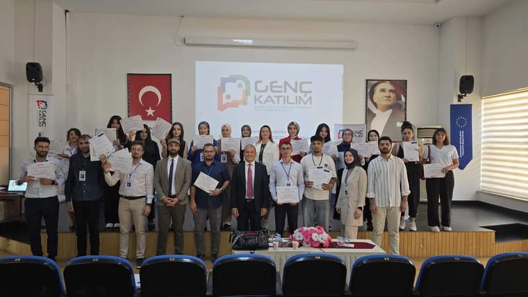 Toplu fotoğrafta gençler ve yetişkinler, ellerindeki belgelerle “Genç Katılım” yazılı sunum önünde duruyor.