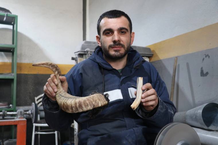 Bir kişi, elinde bir bıçak sapı ve bir boynuz parçası tutuyor, arka planda atölye ekipmanları görünüyor.
