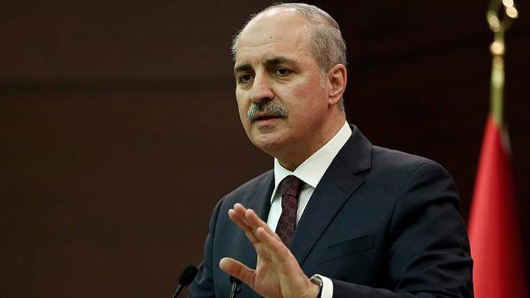 Kürsüde konuşan bir kişi, elini havaya kaldırarak bir şeyler anlatıyor.
