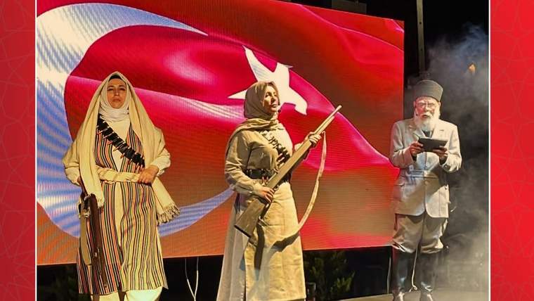 Sahnede tarihî kıyafetler giyen üç kişi, arkalarında Türk bayrağı görüntüsüyle duruyor.