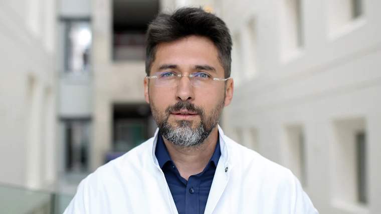 Beyaz önlük giymiş bir doktor, arka planda modern bir bina görünmekte.