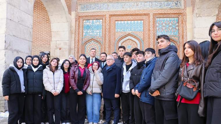 Süslemeli taş yapı girişinin önünde, farklı yaşlarda bir grup kadın ve erkek yan yana duruyor.