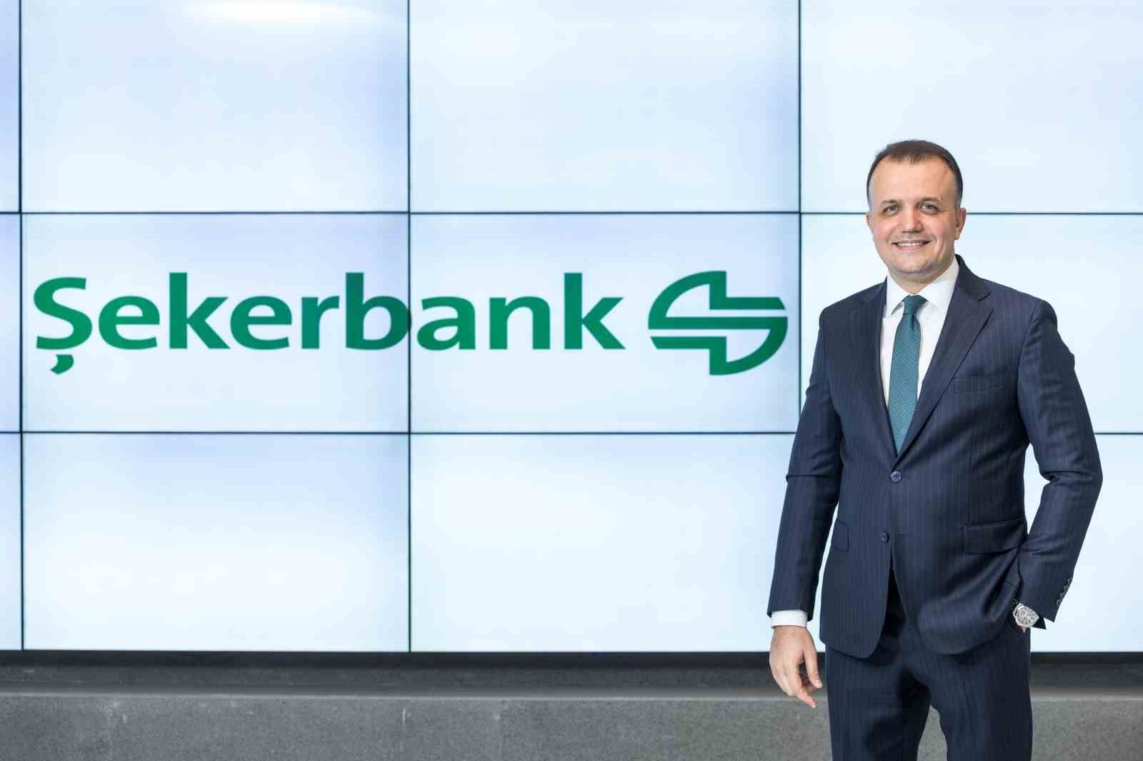 Şekerbank logosunun yer aldığı panonun önünde takım elbiseli bir kişi ayakta duruyor.