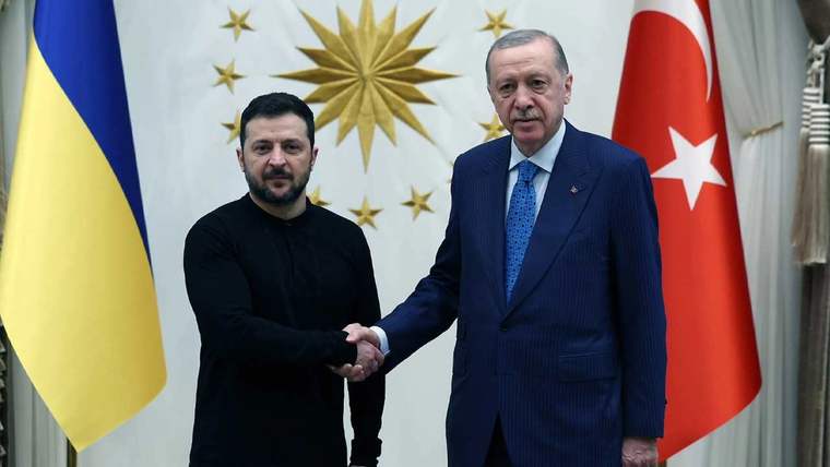 İki erkek bir odada el sıkışıyor; arkalarında Ukrayna ve Türkiye bayrakları ile yıldız motifli duvar bulunuyor.