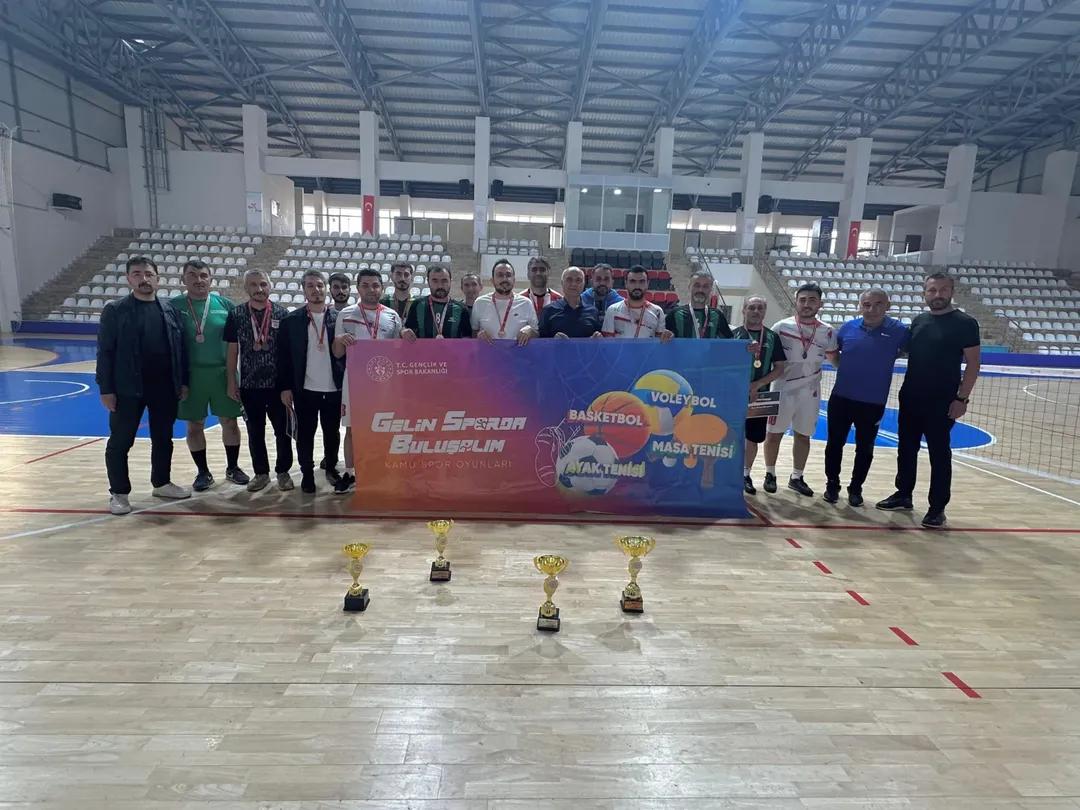 Kapalı spor salonunda bir grup kişi, ellerinde pankartla dört kupanın arkasında yan yana duruyor.