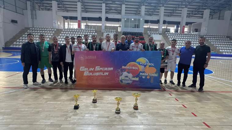 Kapalı spor salonunda bir grup kişi, ellerinde pankartla dört kupanın arkasında yan yana duruyor.