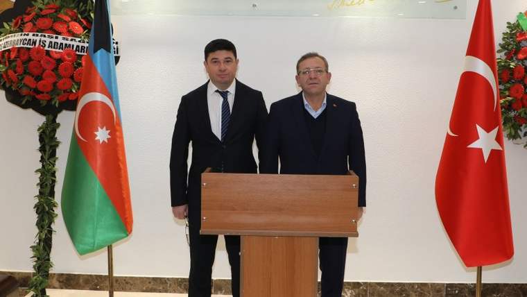 Azerbaycan ve Türkiye bayraklarının önünde, bir masanın arkasında iki kişi duruyor.
