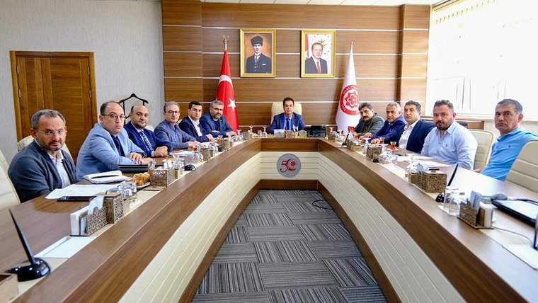Toplantı masasında oturan on bir kişi, arka planda Türk bayrağı ve portreler var.