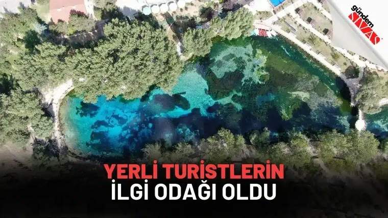 Havadan çekimde, ağaçlarla çevrili turkuaz renkli bir gölet ve çevresindeki yürüyüş yolları görülüyor.