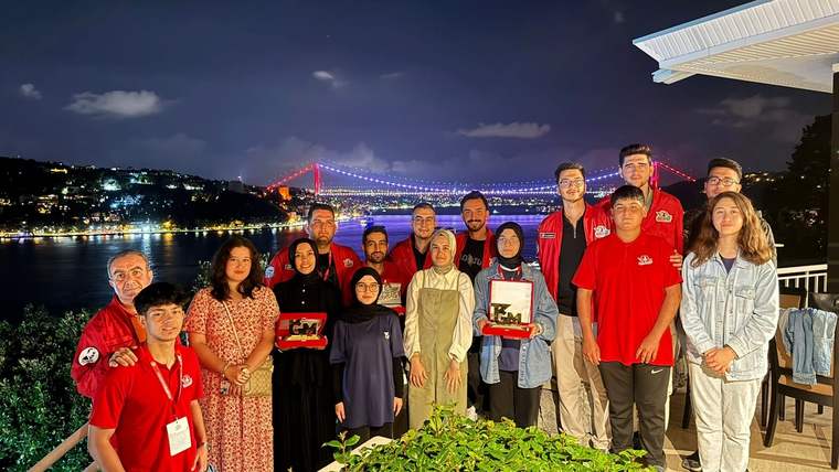 Boğaziçi Köprüsü manzarasında, kırmızı tişörtlü gençler ve yetişkinler bir arada poz veriyor.
