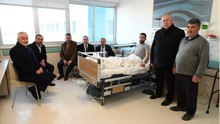 Hastane odasında bir yatak çevresinde oturan ve ayakta duran yedi kişi görülüyor.