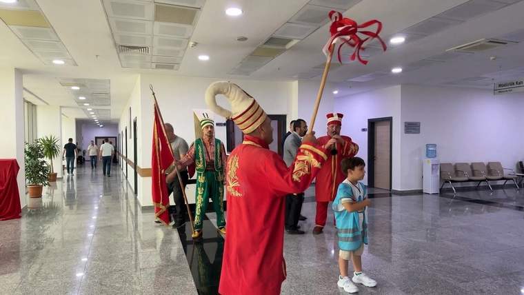 Koridorda kırmızı ve yeşil kostümlü mehteran üyeleri, ellerinde bayrak ve çalgılarla duruyor.