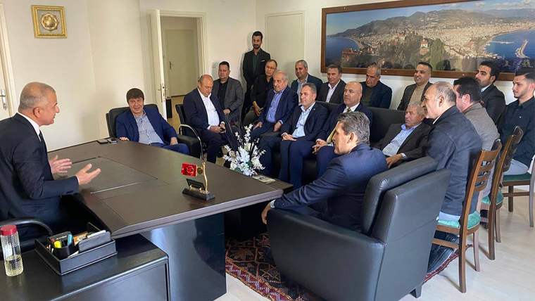 Toplantı odasında masa etrafında oturan bir grup, karşılarındaki konuşmacıyı dinliyor.