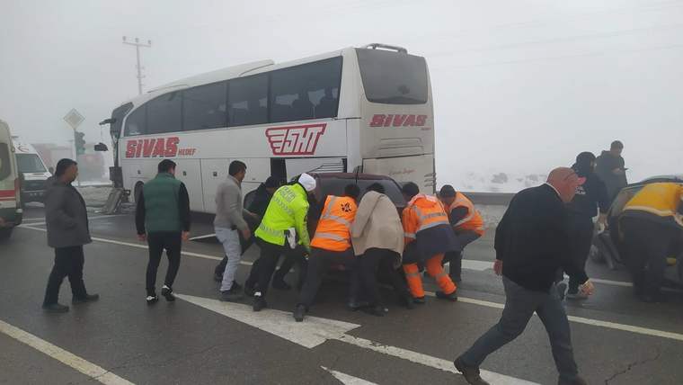 Sisli bir yolda, yolcu otobüsünün etrafında bir grup insan, bir araca yardım ediyor.