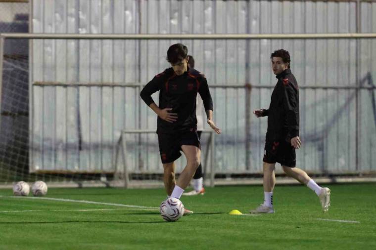 Kapalı sahada iki futbolcu, yeşil zeminde bir futbol topu ve antrenman konileriyle çalışıyor.