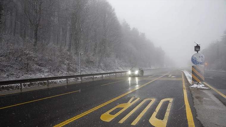 Kar yağışı altında, Bolu Dağı'nda bir araç yolda ilerliyor, yol kenarında uyarı tabelası var.