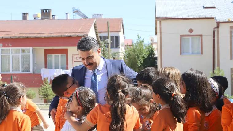 Açık havada bir adam, turuncu tişörtlü çocuklardan oluşan bir grubun arasında duruyor.