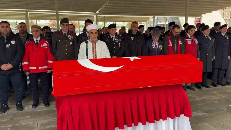Kırmızı örtülü, üzerinde ay yıldız bulunan tabutun çevresinde üniformalı kişiler ve görevliler duruyor.