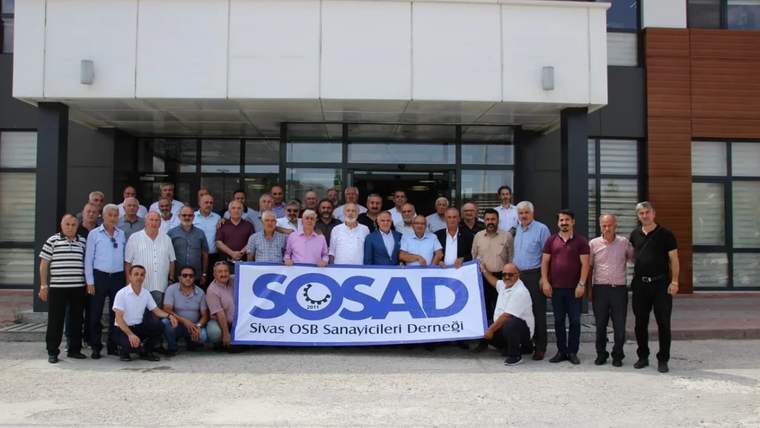 Sivas OSB Sanayicileri Derneği üyeleri, bir binanın önünde toplu halde duruyor ve büyük bir pankart tutuyor.