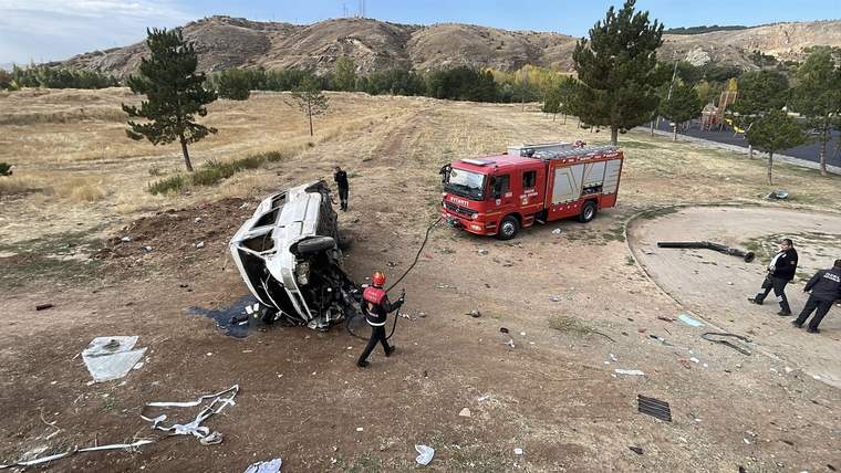Devrilmiş bir minibüs ve yanında itfaiye aracı, çevredeki ağaçlar ve açık alan görünmekte.