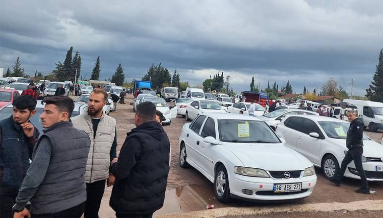Bir araba pazarında çok sayıda araç ve kalabalık bir grup insan yer alıyor.