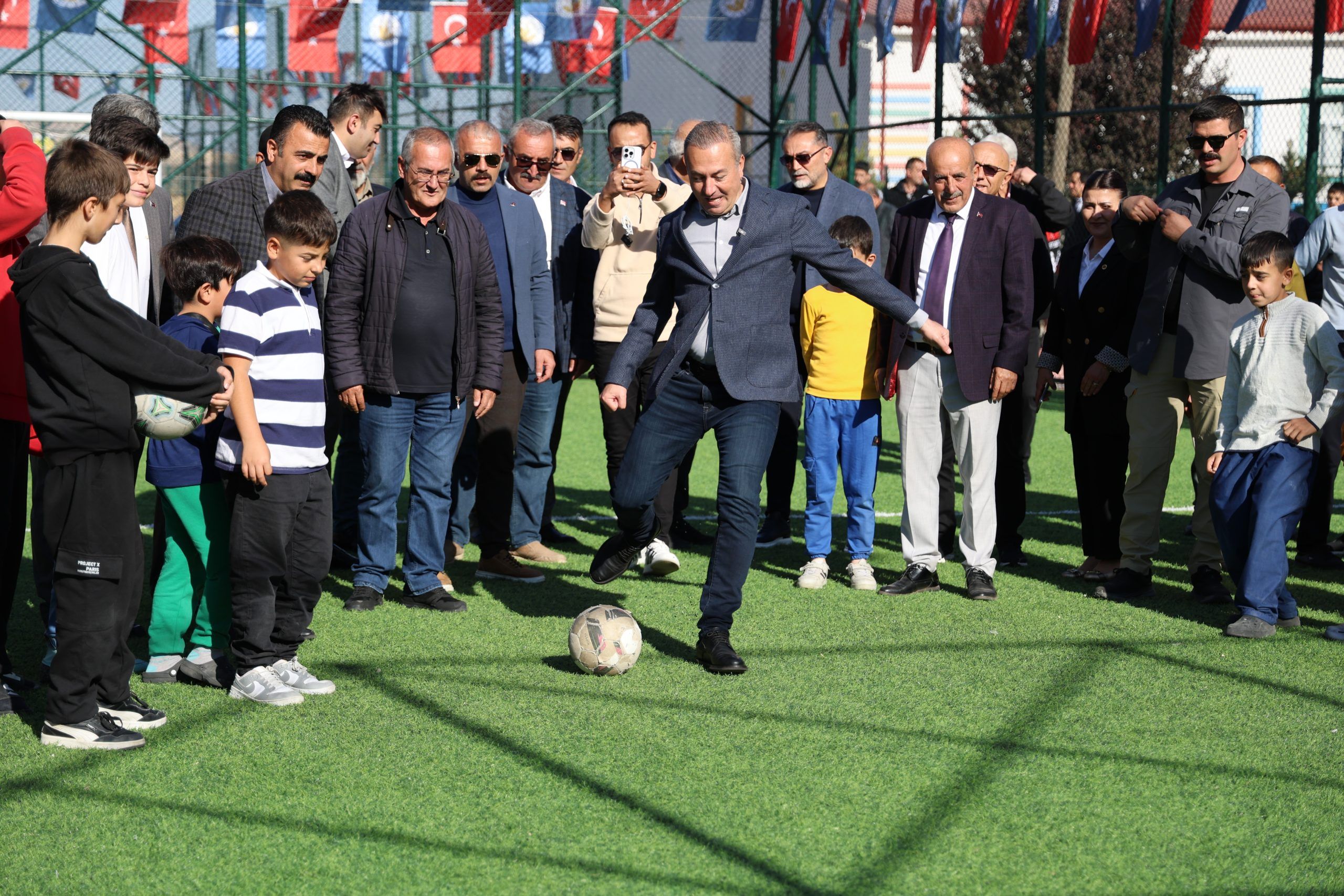 Bir grup insan, yapay çim sahada futbol oynayan bir kişiyi izliyor.