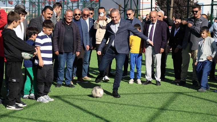Bir grup insan, yapay çim sahada futbol oynayan bir kişiyi izliyor.
